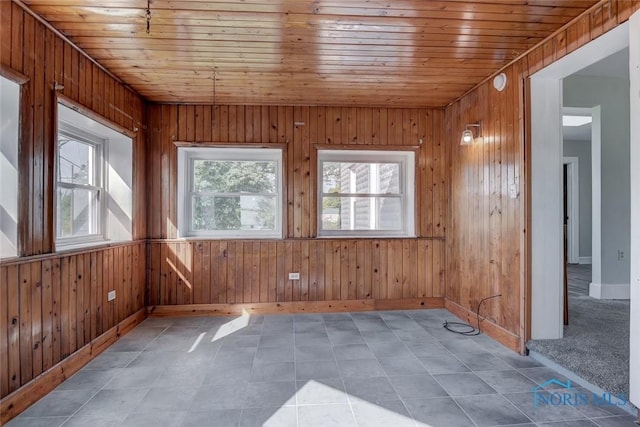 tiled spare room featuring wood walls, baseboards, and wood ceiling