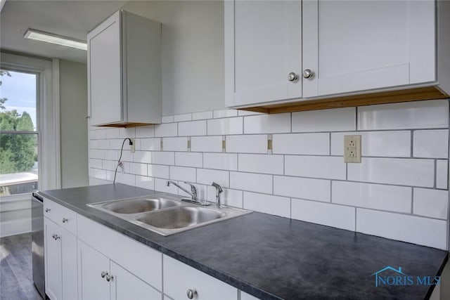 kitchen with a sink, decorative backsplash, dark countertops, and white cabinetry