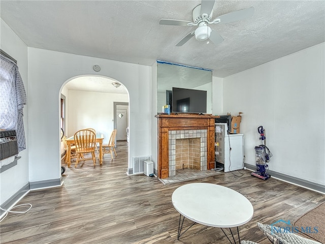 living room featuring ceiling fan, a textured ceiling, hardwood / wood-style floors, and a tile fireplace