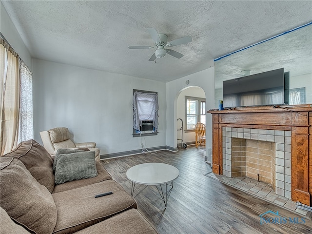 living room featuring a tiled fireplace, a textured ceiling, dark hardwood / wood-style floors, and ceiling fan