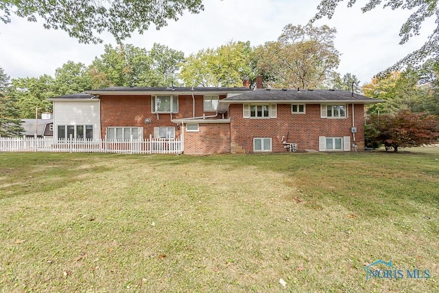 back of house with a yard, brick siding, a chimney, and fence