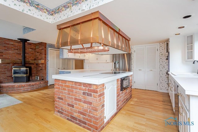 kitchen featuring island range hood, a sink, light countertops, light wood finished floors, and a wood stove