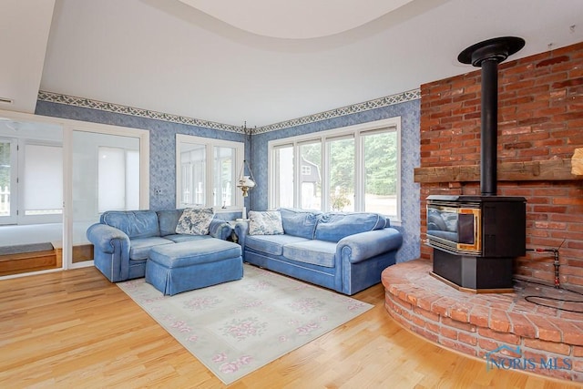 living area with wood finished floors, a wood stove, and wallpapered walls