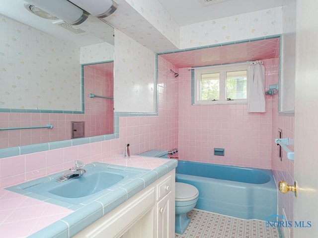 bathroom featuring visible vents, wainscoting, tile walls, and wallpapered walls