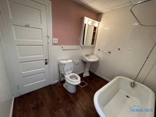 bathroom with a tub, wood-type flooring, tile walls, and toilet