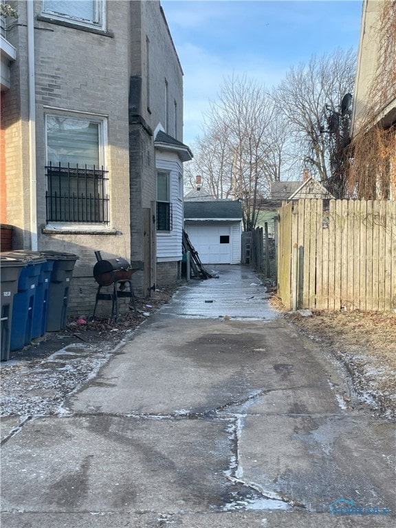 view of side of home featuring concrete driveway, brick siding, fence, and a detached garage