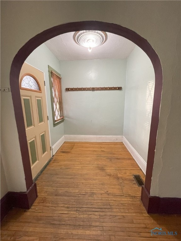 spare room with baseboards, visible vents, arched walkways, and wood finished floors