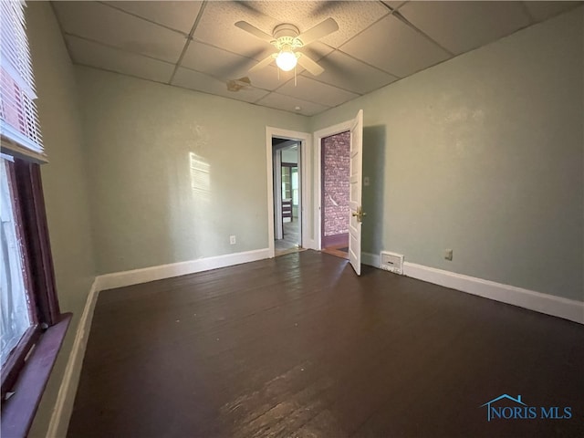 spare room featuring a ceiling fan, dark wood-style flooring, a drop ceiling, and baseboards