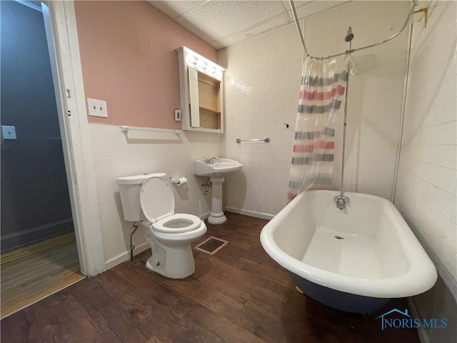 bathroom with visible vents, toilet, wood finished floors, shower / bathtub combination with curtain, and a sink