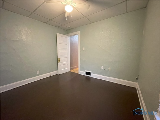 unfurnished room with concrete flooring, a paneled ceiling, and baseboards