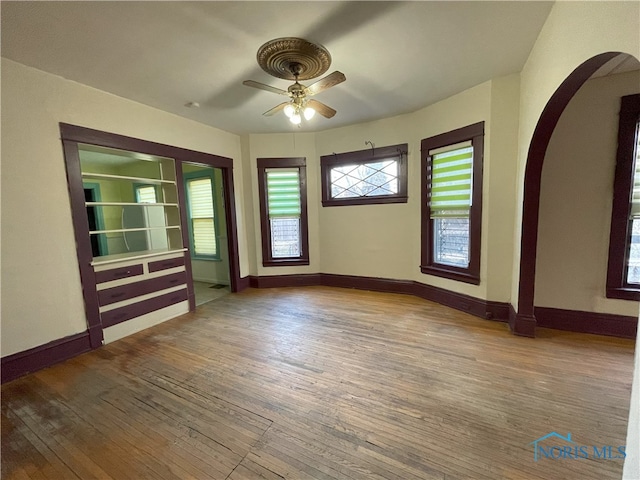 spare room featuring arched walkways, wood finished floors, and baseboards