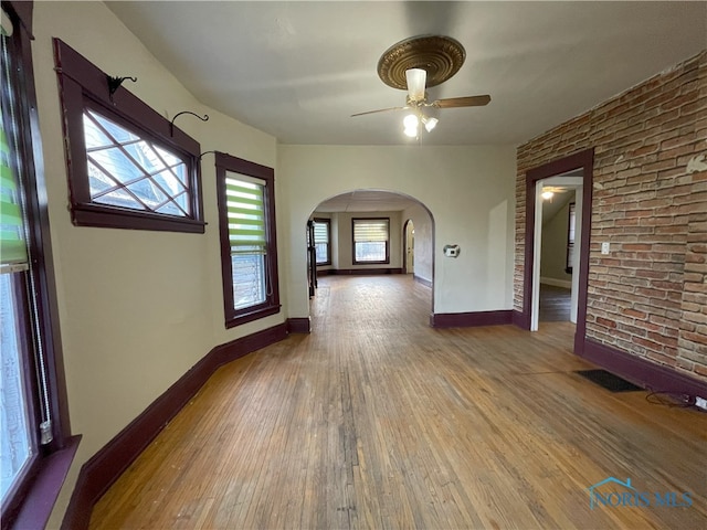 unfurnished room featuring arched walkways, brick wall, wood finished floors, visible vents, and baseboards