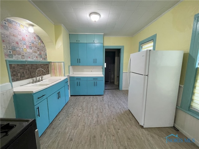 kitchen featuring a sink, light countertops, freestanding refrigerator, light wood finished floors, and crown molding