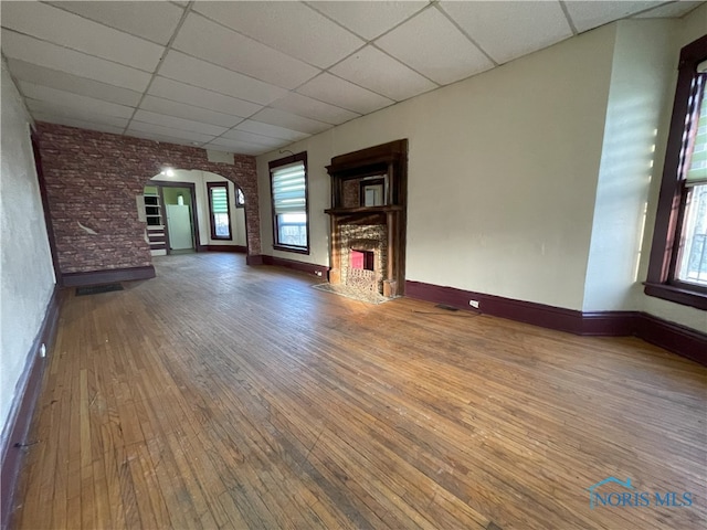 unfurnished living room featuring arched walkways, a drop ceiling, a fireplace with flush hearth, stairway, and wood finished floors