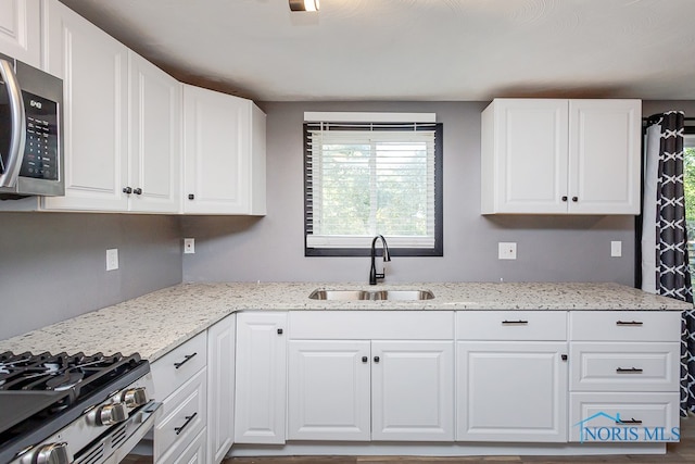 kitchen with hardwood / wood-style flooring, light stone countertops, sink, and white cabinetry