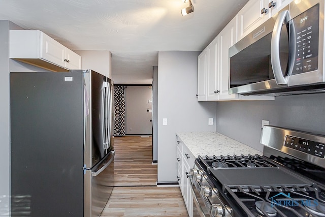 kitchen with light wood-type flooring, white cabinets, appliances with stainless steel finishes, and light stone counters