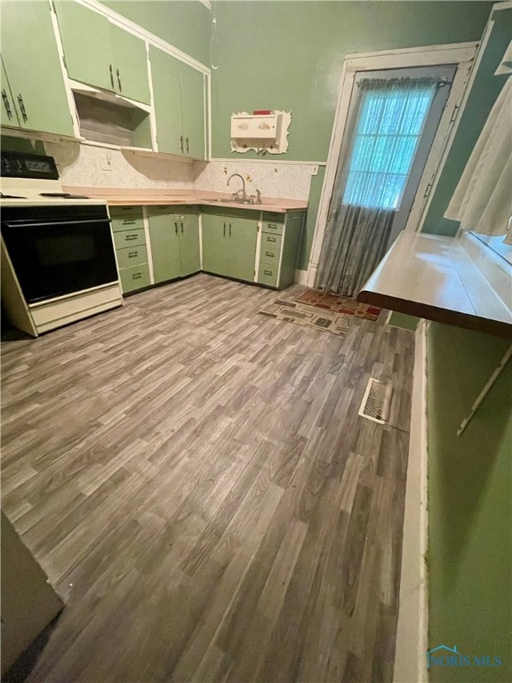 kitchen with electric stove, sink, green cabinetry, and light hardwood / wood-style flooring