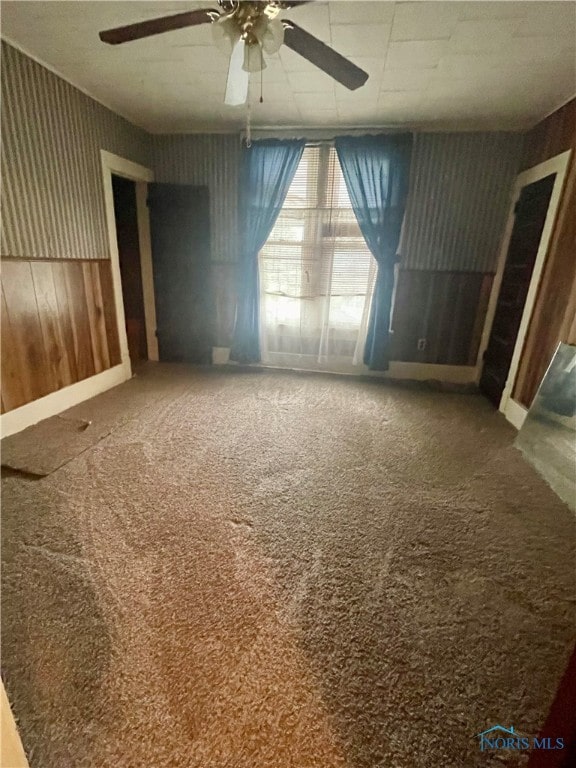 carpeted spare room featuring ceiling fan and wood walls