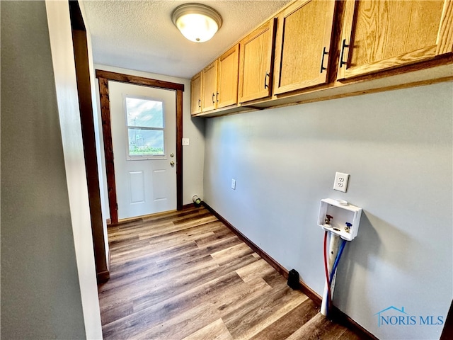 laundry area with hookup for a washing machine, cabinets, light wood-type flooring, and a textured ceiling