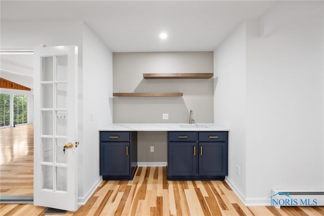 bar featuring light wood-type flooring, blue cabinets, and sink