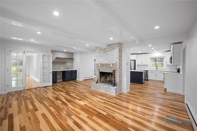 unfurnished living room with beamed ceiling, a fireplace, light hardwood / wood-style floors, and a wealth of natural light