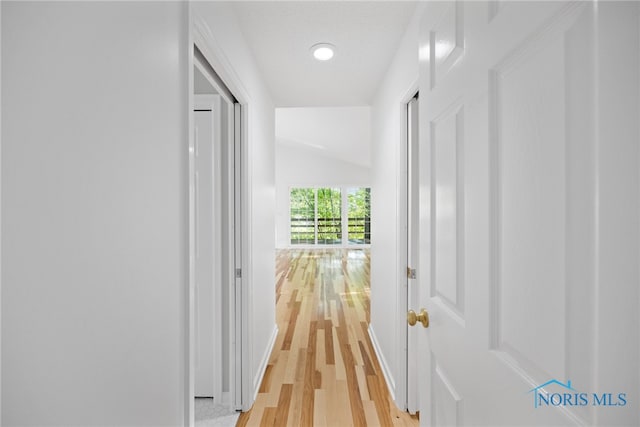 corridor with light hardwood / wood-style floors and vaulted ceiling