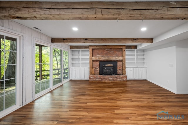 unfurnished living room with beamed ceiling, a fireplace, wood walls, and hardwood / wood-style flooring