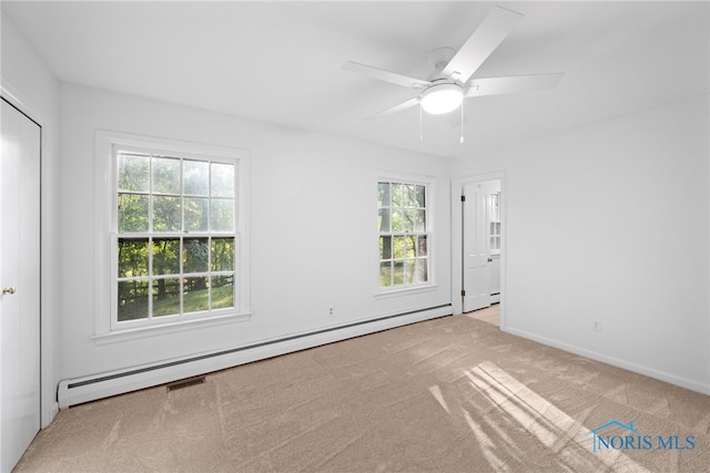 carpeted empty room featuring a baseboard heating unit, ceiling fan, and a healthy amount of sunlight