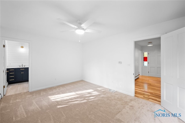 unfurnished bedroom featuring ceiling fan, sink, a baseboard radiator, light wood-type flooring, and ensuite bathroom