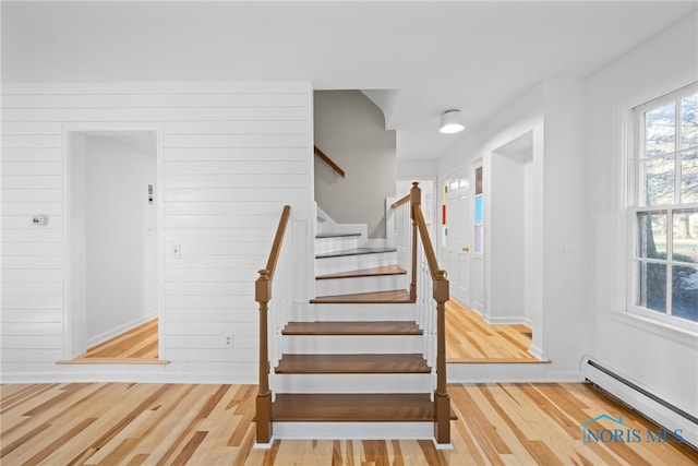 staircase with wood walls, baseboard heating, and hardwood / wood-style floors