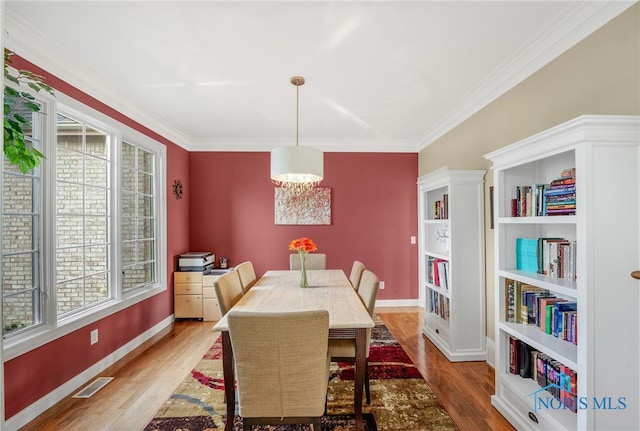 dining room with light wood-type flooring, a healthy amount of sunlight, and ornamental molding