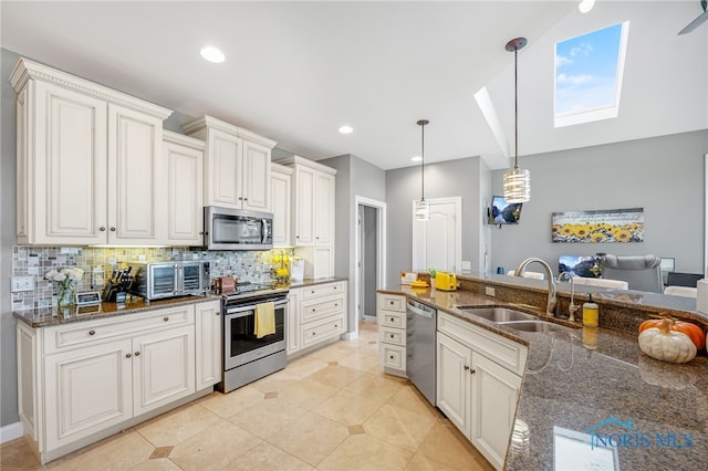 kitchen featuring sink, white cabinetry, stainless steel appliances, decorative light fixtures, and dark stone countertops