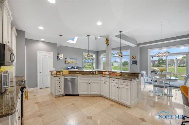 kitchen featuring decorative light fixtures, a center island with sink, white cabinetry, appliances with stainless steel finishes, and dark stone counters