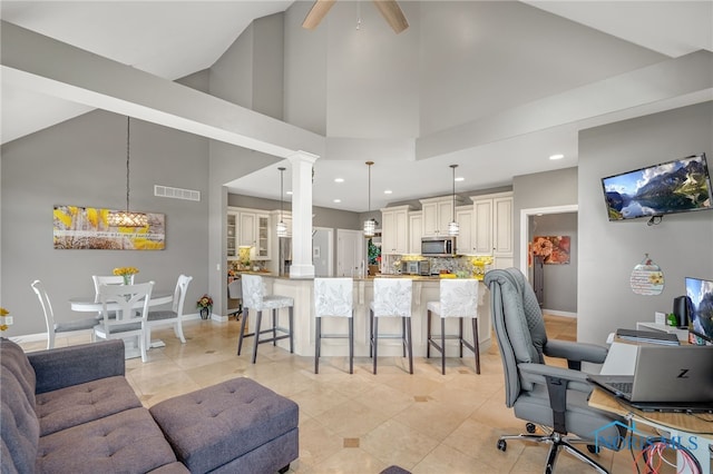 tiled living room with ceiling fan, ornate columns, and high vaulted ceiling