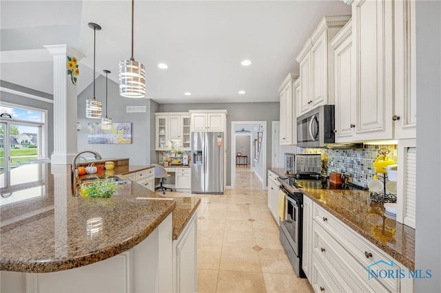 kitchen featuring appliances with stainless steel finishes, white cabinets, pendant lighting, dark stone counters, and sink