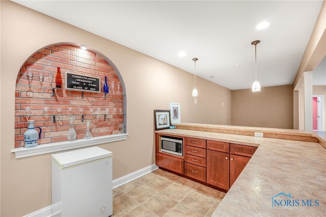 kitchen with fridge, light tile patterned flooring, decorative light fixtures, and stainless steel microwave