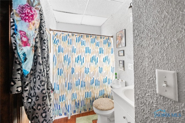 bathroom with hardwood / wood-style floors, a drop ceiling, vanity, and toilet