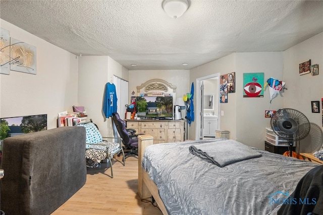 bedroom featuring light wood-type flooring, a textured ceiling, and connected bathroom