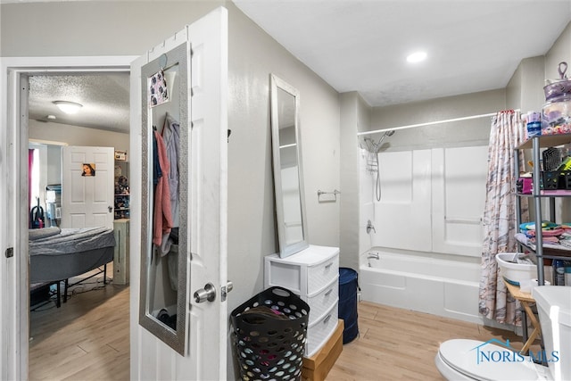 bathroom with a textured ceiling, toilet, shower / bathtub combination with curtain, and hardwood / wood-style floors