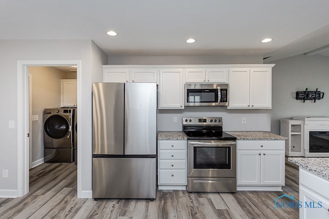 kitchen with light stone counters, white cabinets, wood-type flooring, appliances with stainless steel finishes, and washer / dryer