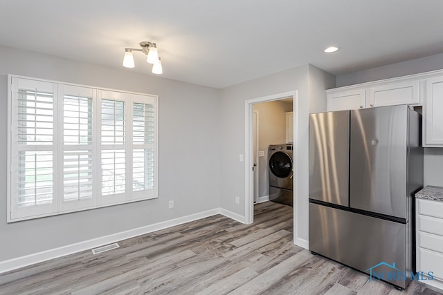 kitchen with white cabinets, washer / clothes dryer, light wood-type flooring, and stainless steel fridge