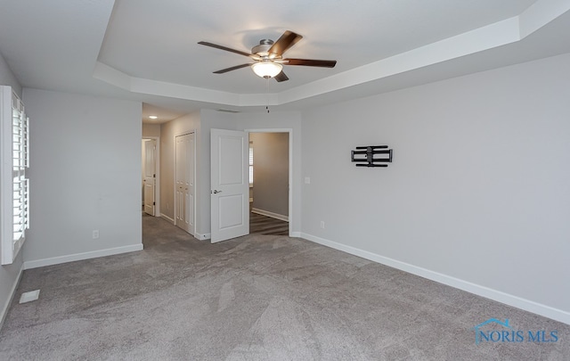 unfurnished room featuring ceiling fan, a tray ceiling, and light carpet