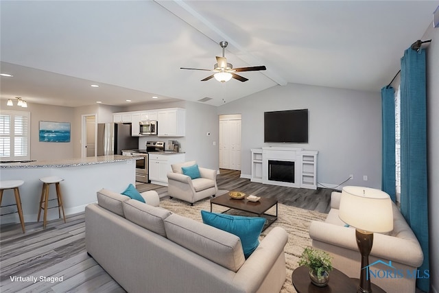 living room featuring ceiling fan, light hardwood / wood-style flooring, lofted ceiling with beams, and a fireplace