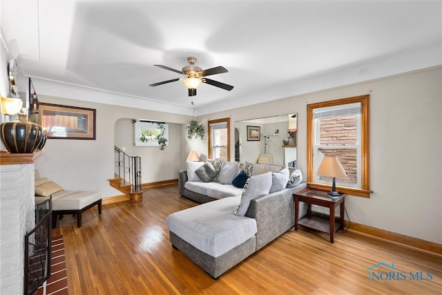 living room with wood-type flooring, ceiling fan, and a brick fireplace