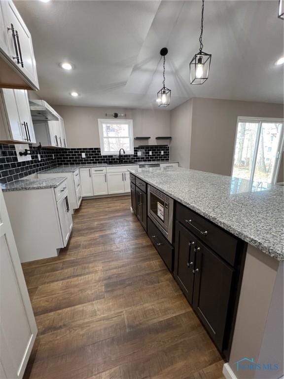 kitchen featuring sink, stainless steel microwave, light stone countertops, white cabinets, and decorative light fixtures