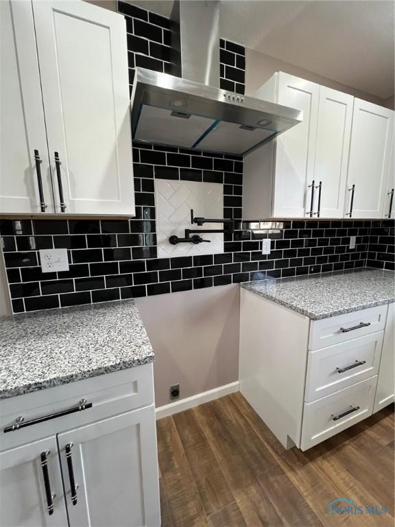 kitchen featuring light stone countertops, wall chimney range hood, white cabinets, and backsplash