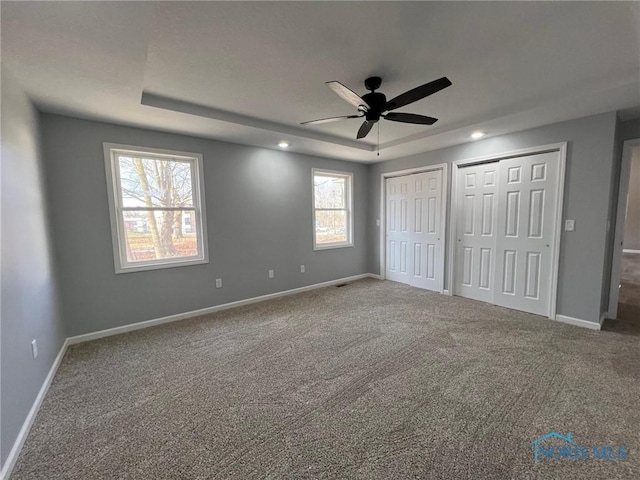 unfurnished bedroom with a raised ceiling, carpet, multiple closets, and ceiling fan