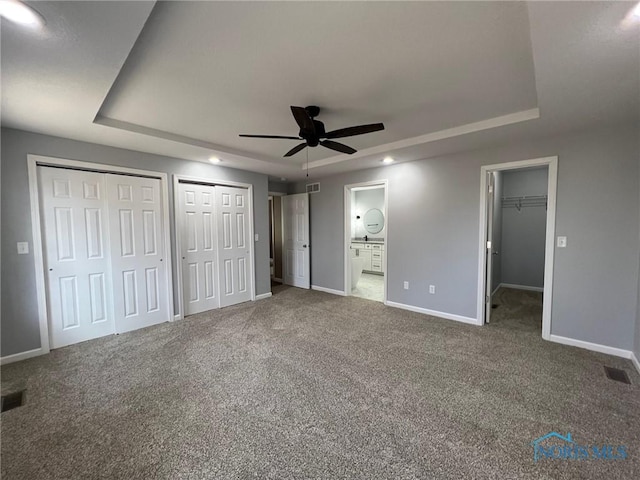 unfurnished bedroom with multiple closets, ceiling fan, ensuite bathroom, and a raised ceiling