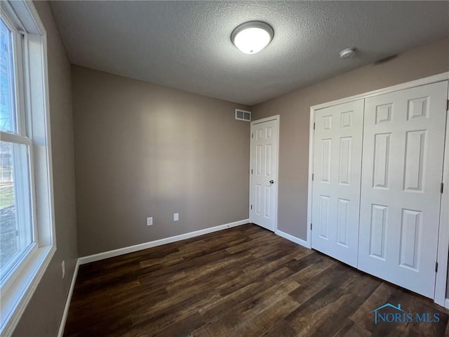 unfurnished bedroom featuring dark wood-type flooring, a textured ceiling, and a closet