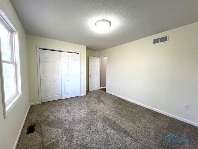 unfurnished bedroom featuring multiple windows, carpet floors, a closet, and a textured ceiling